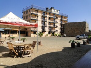 Relax in the hotel's outdoor seating area, surrounded by lush potted plants and comfortable chairs under a shaded canopy.