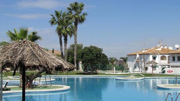 A swimming pool with palm trees and a thatched-roof structure. - Ground floor bungalow LAGO JARDIN, LOS BALCONES, TORREVIEJA (Torrevieja)