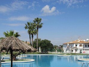 Una piscina con palmeras y una estructura de techo de paja.