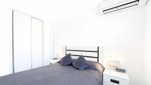 A bedroom with a bed, bedside tables, a nightstand, a wall-mounted air conditioner, and a wardrobe. - Ground floor bungalow LAGO JARDIN, LOS BALCONES, TORREVIEJA (Torrevieja)