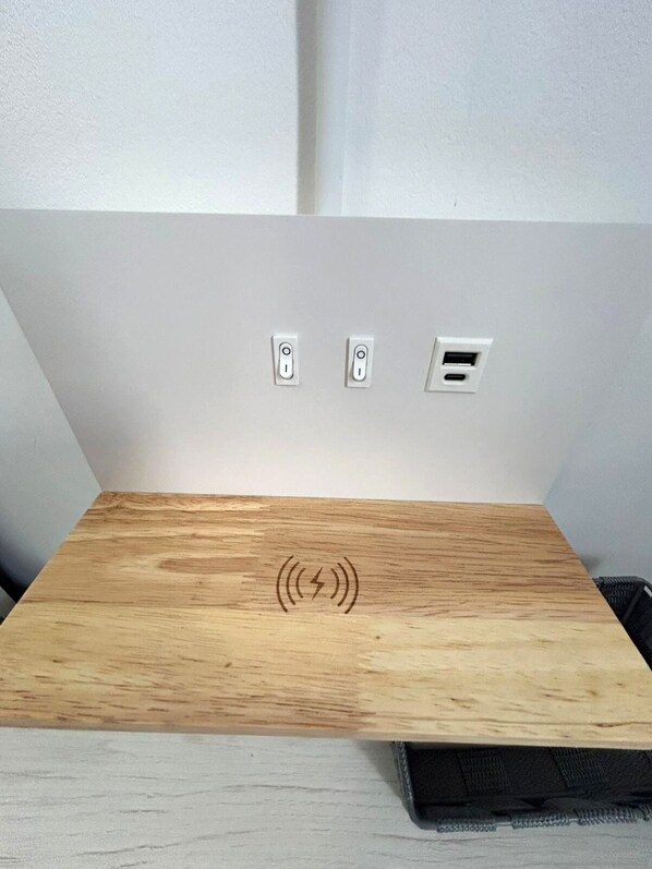 Una mesa de madera con un símbolo de carga inalámbrica, dos interruptores y un puerto USB en una pared blanca.
