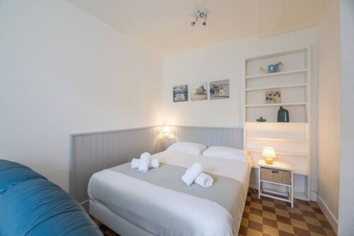 A hotel room with a bed, bedside tables, a shelf with items, and a wall with pictures.