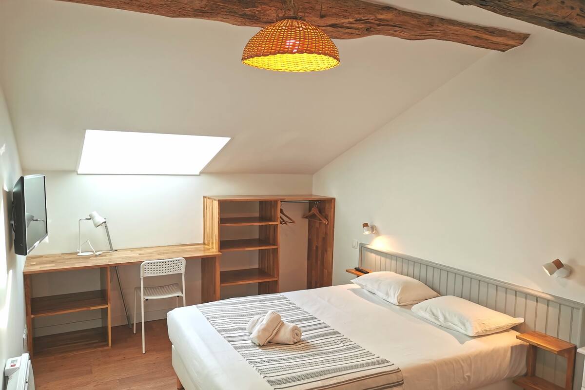 A bedroom with a bed, desk, chair, and a hanging light fixture.