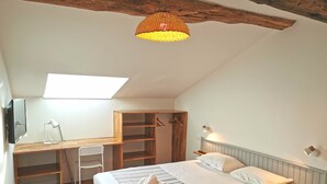 A bedroom with a bed, desk, chair, and a hanging light fixture.