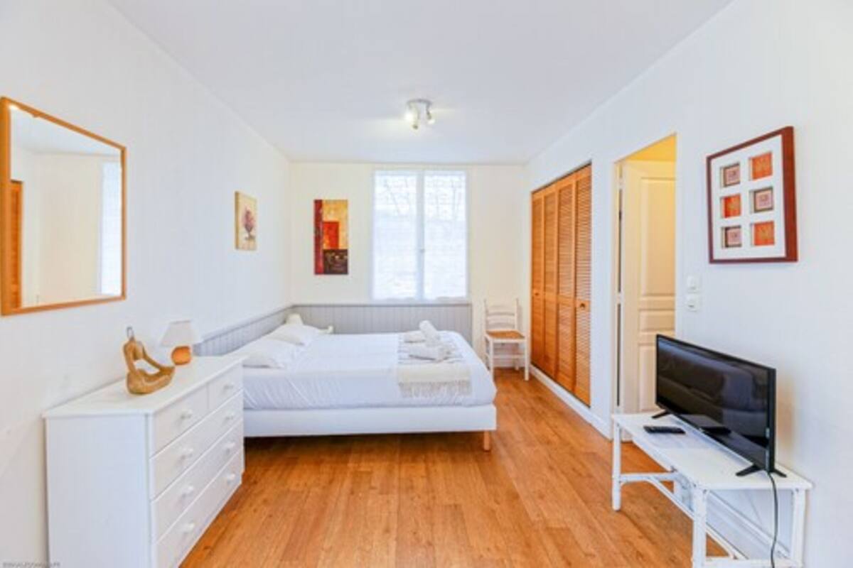 A bedroom with a bed, a dresser, a TV, and a window.