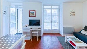 A room with a desk, chair, and a sofa. There are windows and a radiator.