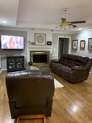 A living room with a leather sofa, a television, a fireplace, and framed pictures on the wall.