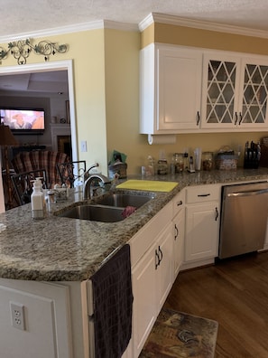 A kitchen with granite countertops, white cabinets, a stainless steel sink, and a built-in dishwasher.