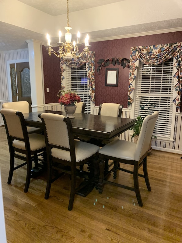A dining room with a dark wooden table and matching chairs, a chandelier, and a floral-patterned wall.
