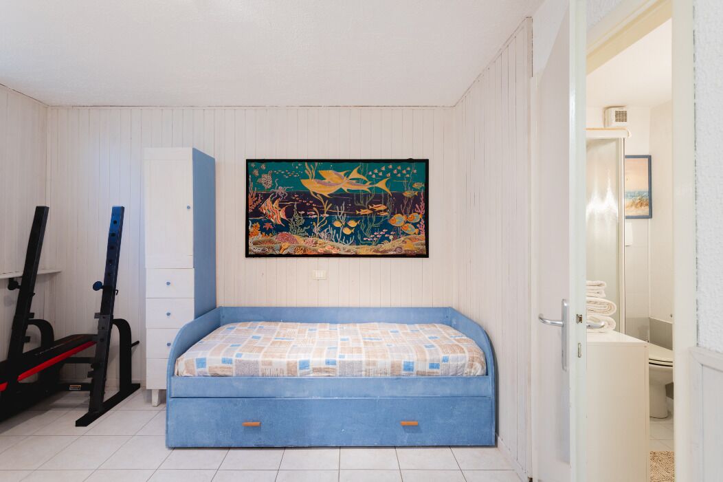 A bedroom with a bed, a painting, a door, and a white cabinet.