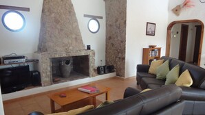 Un saló amb una llar de pedra, un sofà de cuir negre, una taula de centre de fusta i una prestatgeria.