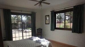 Una habitació amb un llit, una cadira, una taula amb una làmpada i una finestra amb cortines.