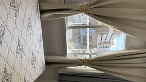 A room with a patterned wall, a window with curtains, and a view of a cityscape. - Lindo apto 70 m do mar (Centro)