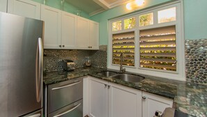 A kitchen with white cabinets, a stainless steel refrigerator, a granite countertop, and a window with a mosaic design.