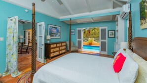A bedroom with a four-poster bed, a ceiling fan, a view of a pool, and a door leading to another room.