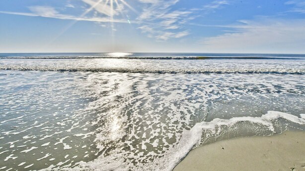 Une plage avec des vagues, un ciel dégagé et un soleil bien visible.