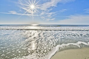 Een strand met golven, een heldere lucht en een zichtbare zon.