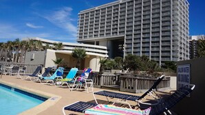 Un espace piscine d’hôtel avec des chaises longues et un panneau indiquant une zone peu profonde où il est interdit de plonger.