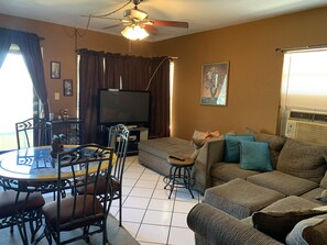 A living room with a sofa, a dining table with chairs, a ceiling fan, a television, and a window with curtains. - Condo with a Beautiful View (Pompano Beach)
