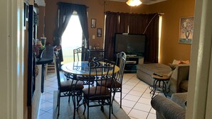 Een woonkamer met een eettafel, stoelen, een bank, een televisie en een plafondventilator.