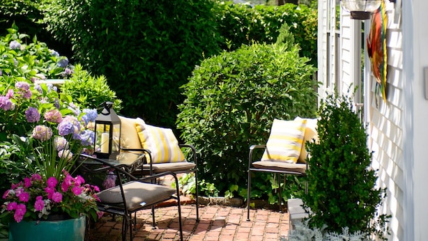 Une terrasse avec deux chaises et une table, entourée de plantes en pot et bordée d’un chemin en briques.