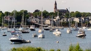 Un port de plaisance où sont amarrés différents types de bateaux, un imposant beffroi en arrière-plan et des bâtiments le long de la rive.