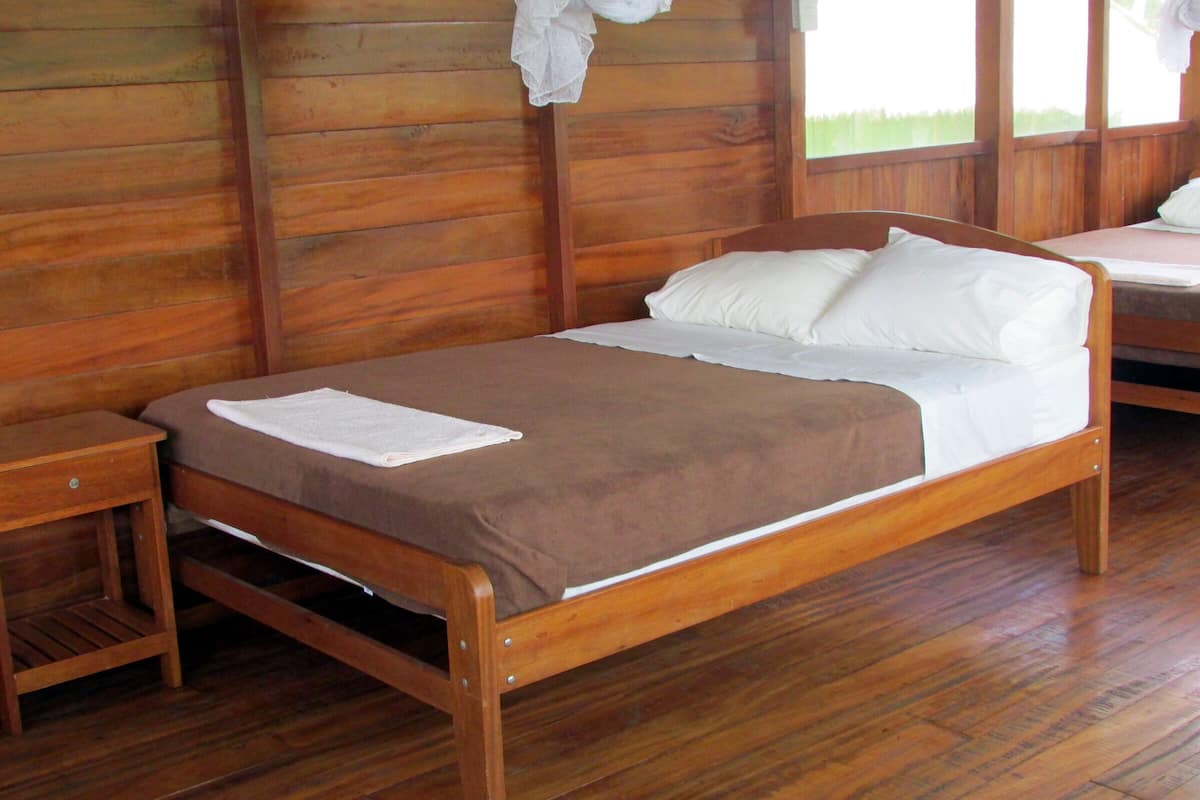 A wooden bed with a brown bedspread and white pillows in a room with wooden walls and floors.
