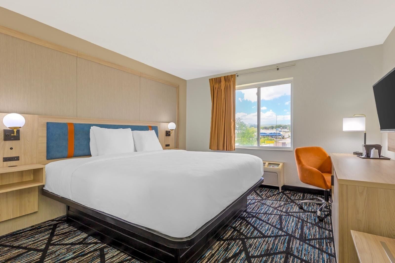 Habitación de hotel con una cama grande, un escritorio, una silla, un ventanal con vistas y un televisor de pantalla plana.
