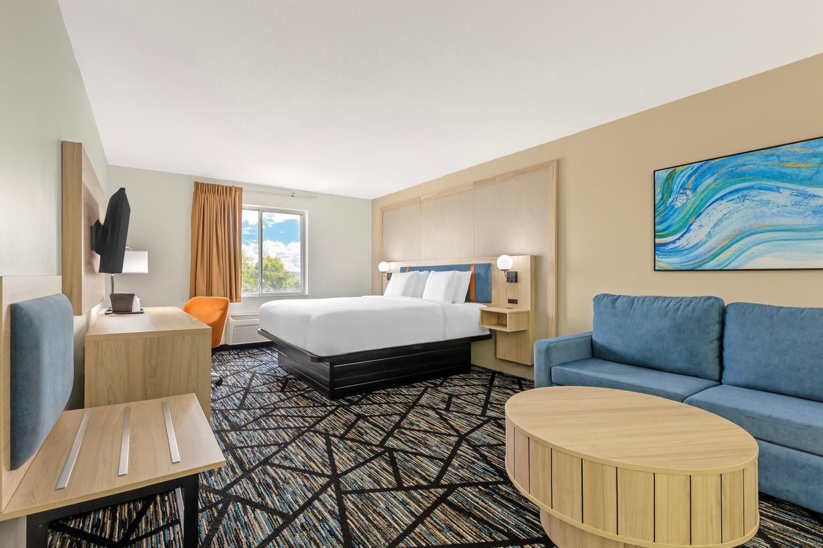 Une chambre d’hôtel avec un lit, un bureau, une chaise, un canapé et un tableau au mur.