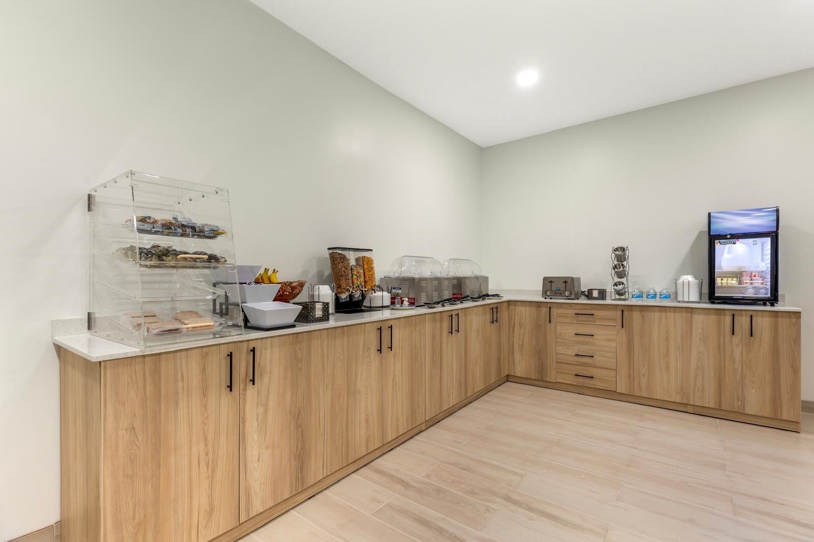 A modern kitchen with wooden cabinets, a glass display case, and various food items.