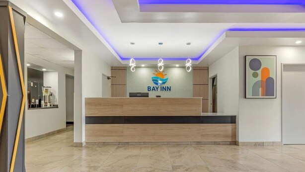 Uma área de recepção de hotel com um balcão de madeira, um logotipo acima e uma obra de arte abstrata emoldurada na parede.