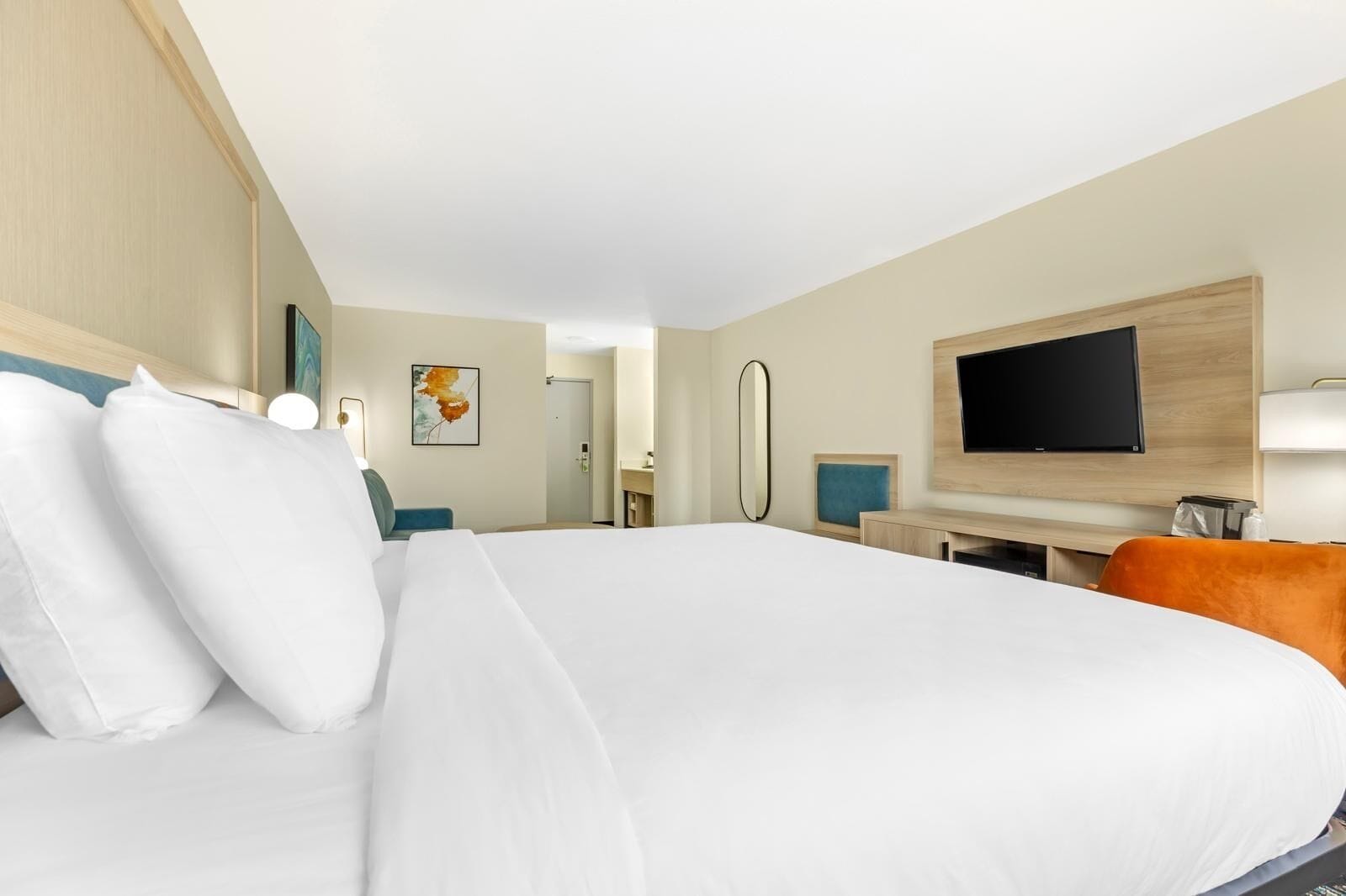 A hotel room with a large bed, a desk with a chair, a television, and a mirror.