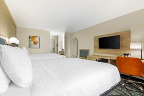 Una habitación de hotel con una cama grande, un escritorio con computadora, una televisión y una silla.