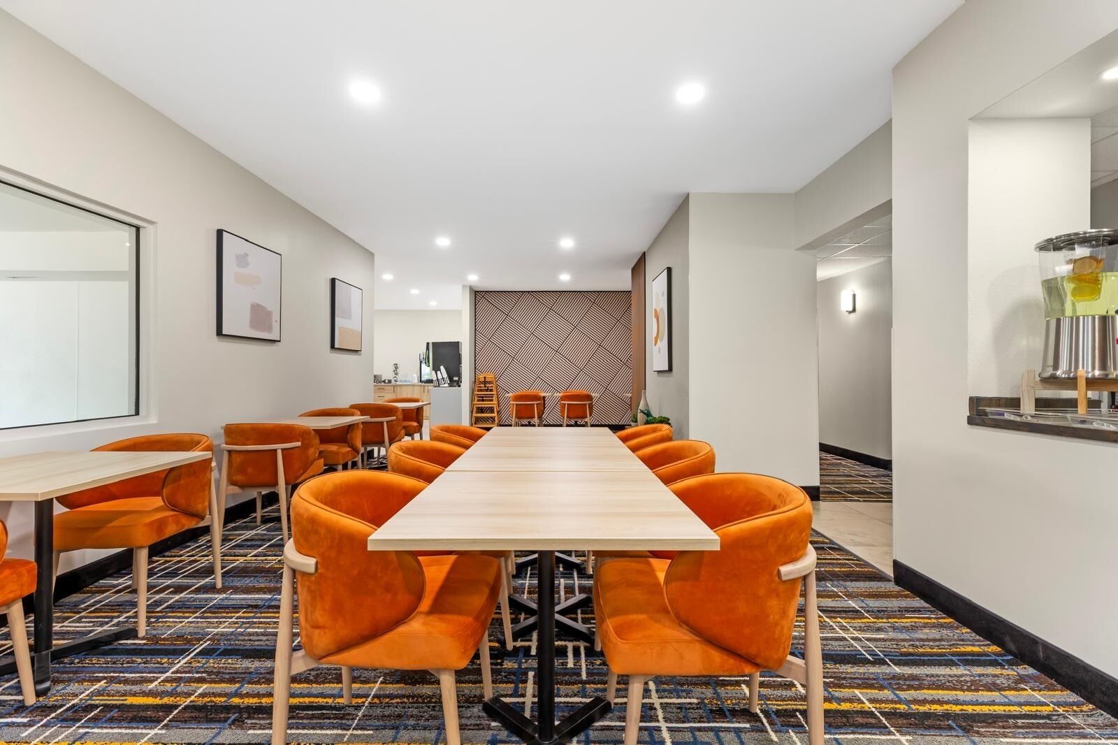 A conference room with a long table and orange chairs, a patterned carpet, and a modern wall design.