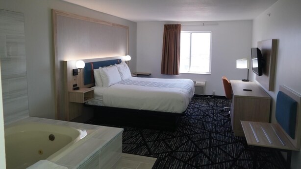A hotel room with a bed, a desk, a chair, a TV, a window, and a bathroom with a bathtub. - Bay Inn & Suites Troy (Troy)