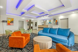 A hotel lobby with a reception desk, a blue sofa, and orange armchairs. - Bay Inn & Suites Troy (Troy)