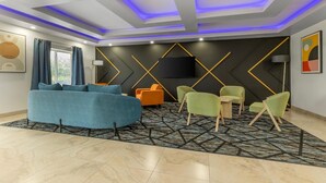 A modern living room with a sofa, chairs, a flat-screen TV, and a patterned rug. - Bay Inn & Suites Troy (Troy)