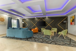 A modern living room with a sofa, chairs, a flat-screen TV, and a patterned rug. - Bay Inn & Suites Troy (Troy)