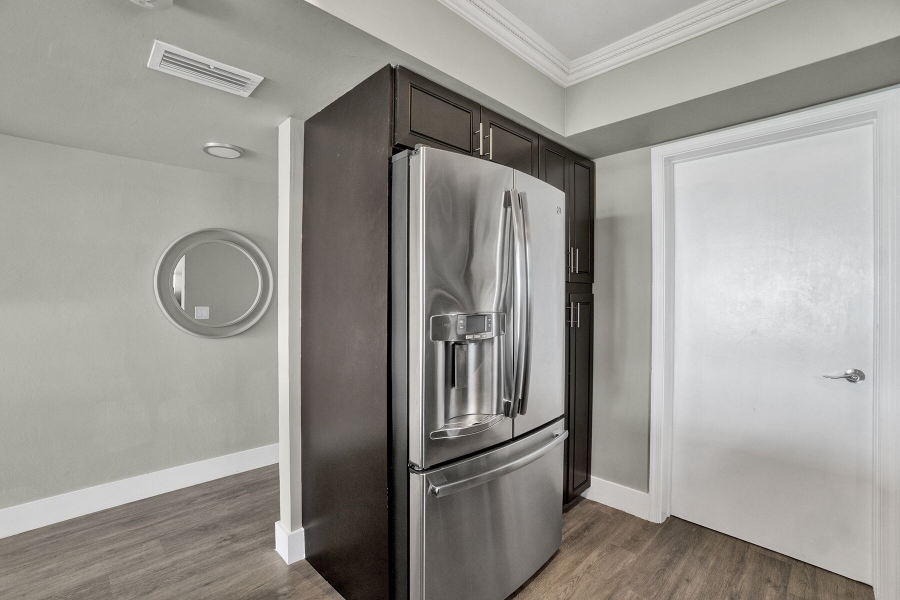 A modern kitchen with a stainless steel refrigerator, dark wooden cabinets, and a white door.