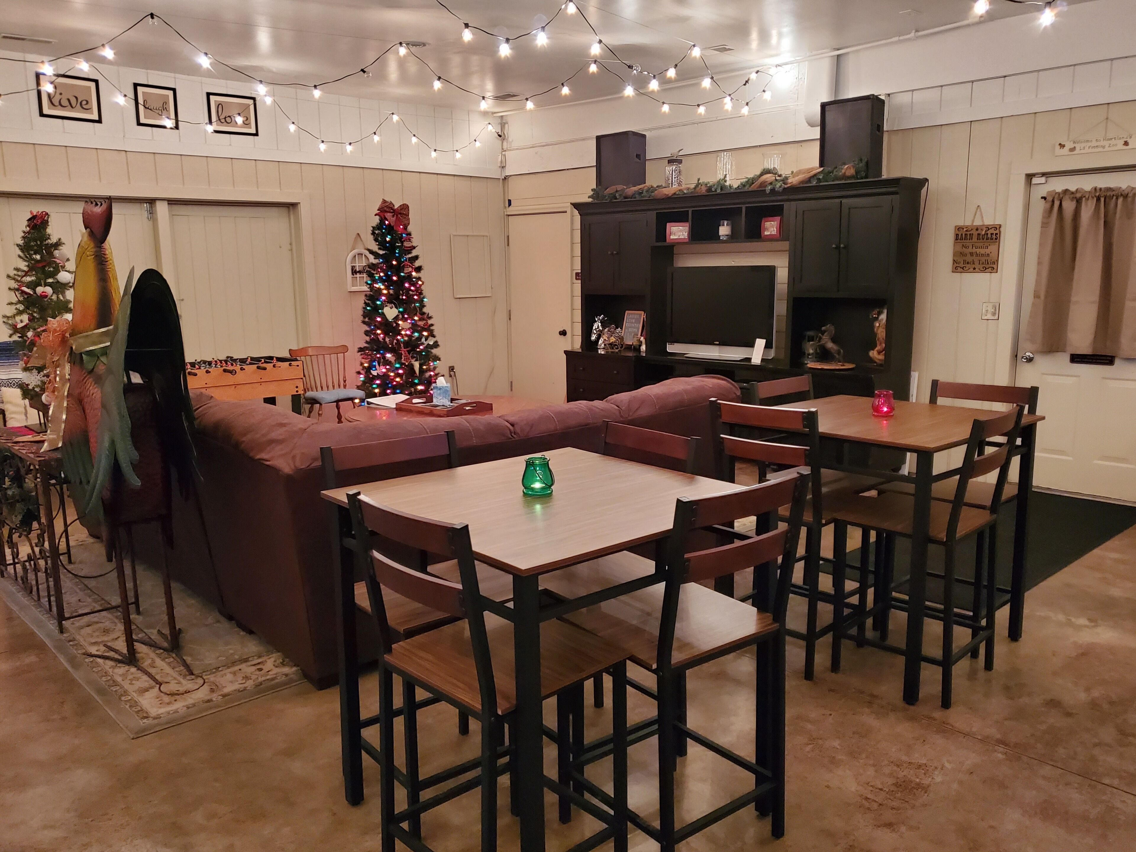 Un salon chaleureux avec un canapé marron, une table à manger en bois et des chaises. Un sapin de Noël est décoré de guirlandes lumineuses et d’ornements.