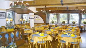 Un espace repas comprenant plusieurs tables et chaises, décoré de nappes jaunes et agrémenté de centres de table floraux.