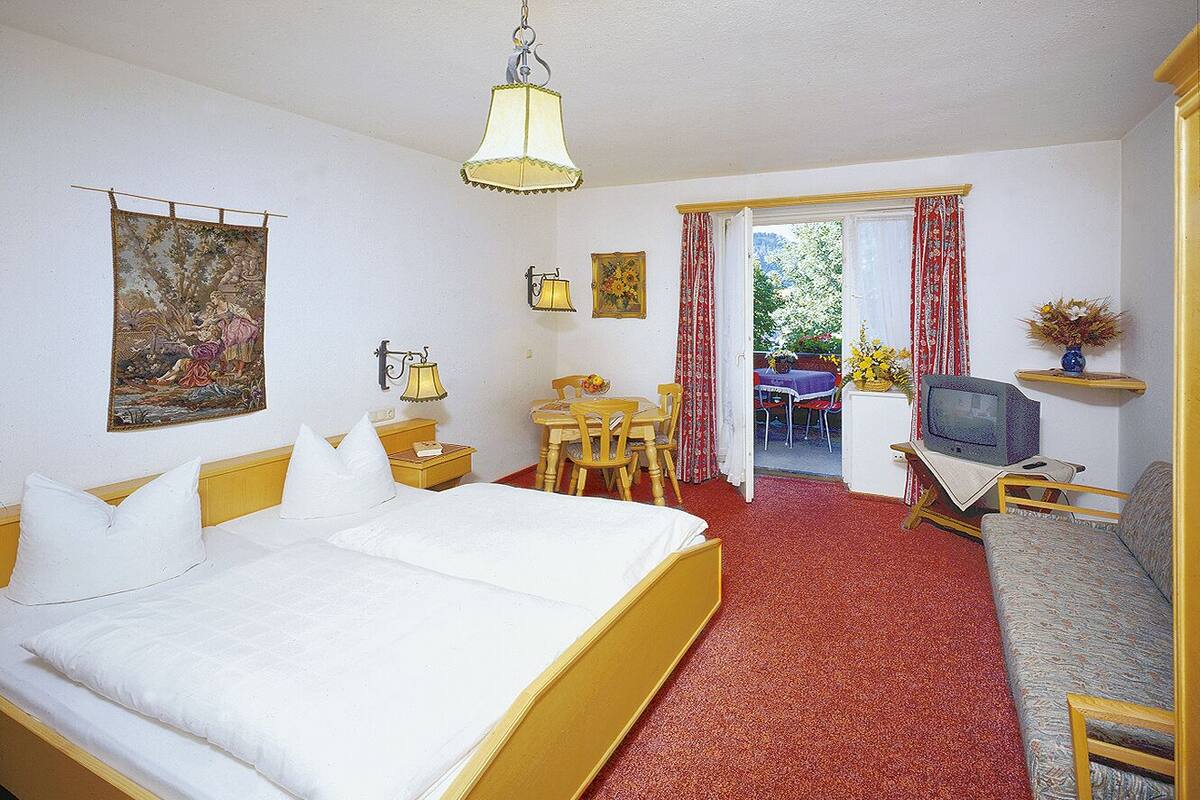 Een hotelkamer met een bed, een bank, een televisie, een bureau met stoel en een raam met gordijnen.