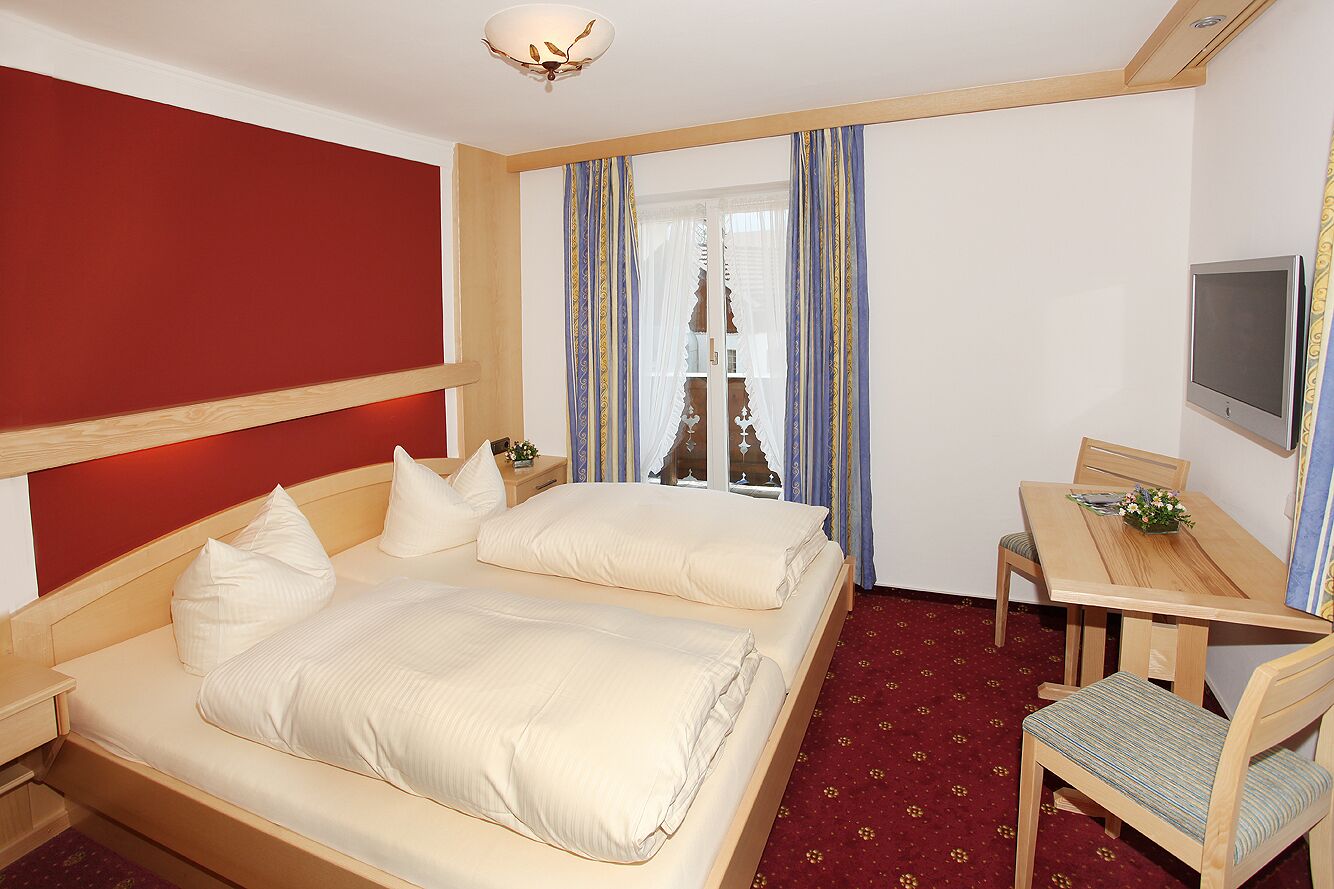 Une chambre d’hôtel avec deux lits, un bureau, une chaise, une télévision et une fenêtre avec des rideaux.