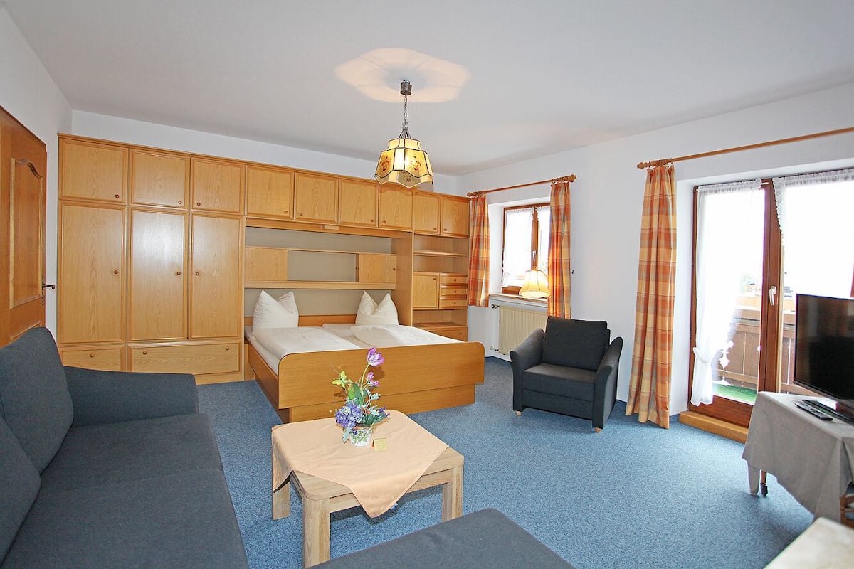 Een slaapkamer met een bed, een bank, een stoel, een televisie en een tafel met een vaas.