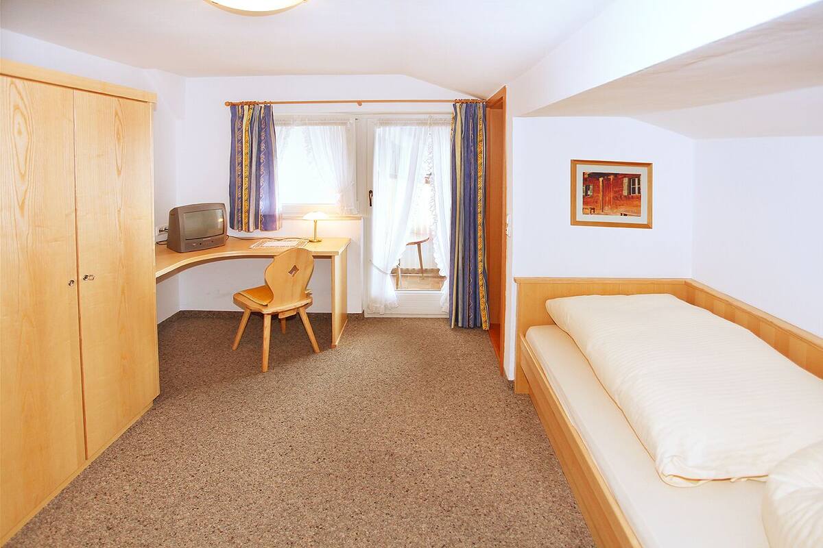 Een kamer met een bed, een bureau met stoel, een televisie en een raam met gordijnen.