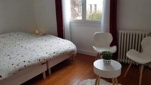 Ein Schlafzimmer mit einem Bett, zwei Stühlen, einem kleinen Tisch mit einer Pflanze und einer Heizung.