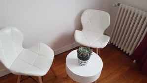 Zwei weiße Stühle mit einem runden Tisch dazwischen, ein Sukkulenten im Topf auf dem Tisch und eine Heizung im Hintergrund.