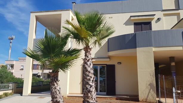 A modern two-story house with a flat roof, a balcony, and a small garden area with palm trees. - Residence Ionian (Gallipoli)