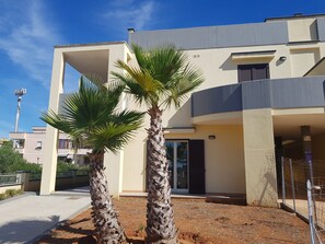 A modern two-story house with a flat roof, a balcony, and a small garden area with palm trees. - Residence Ionian (Gallipoli)
