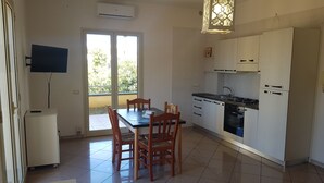 A modern kitchen with white cabinets, a gas stove, and a built-in oven. There is a dining table with chairs and a small refrigerator. - Residence Ionian (Gallipoli)